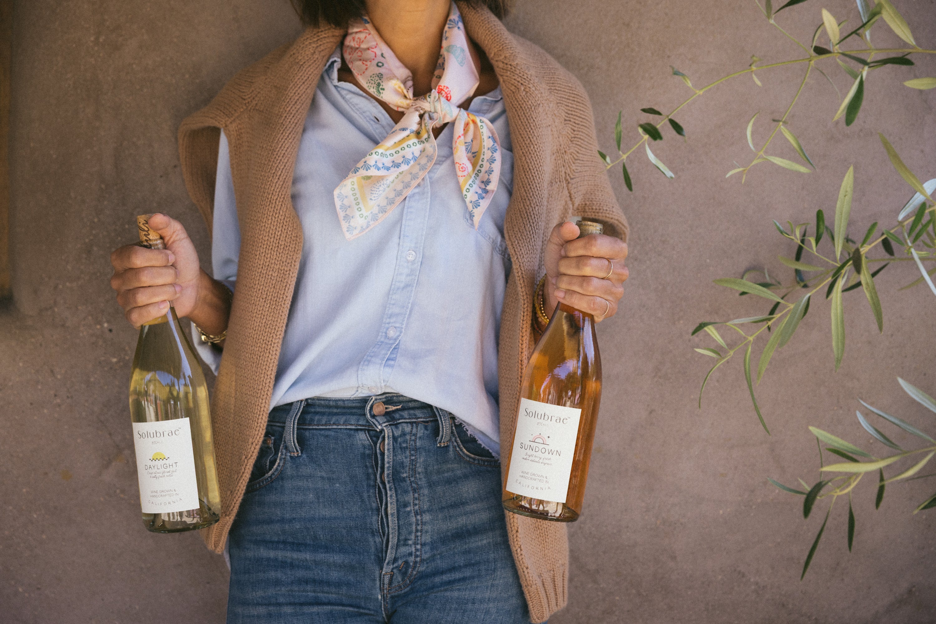 Woman holding Solubrae DAYLIGHT and SUNDOWN alcohol-removed wine bottles in California vineyard
